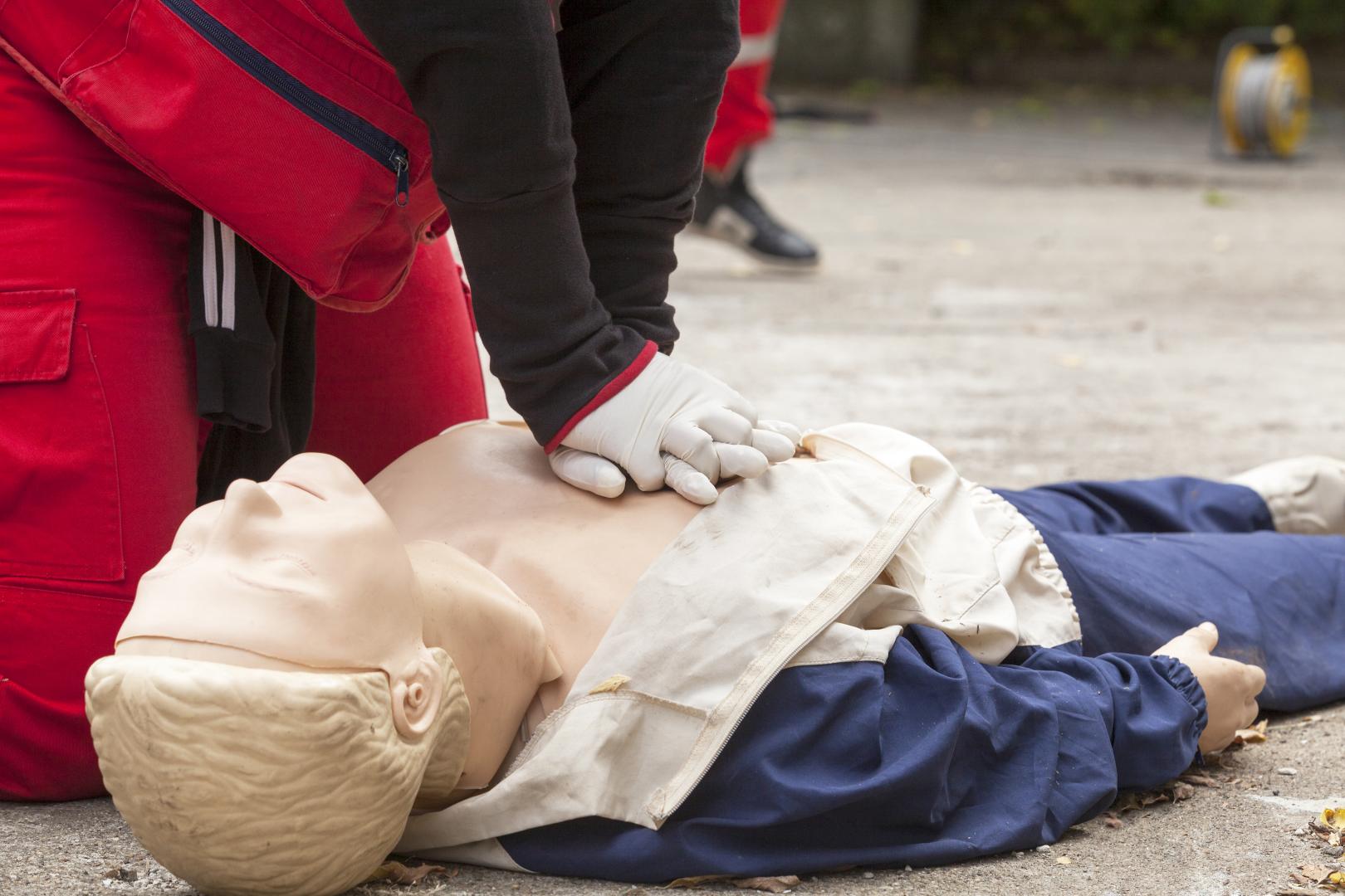 Two hands reach down to perform CPR on a training dummy.