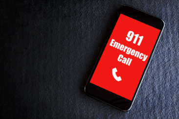 A cell phone with a red screen and white lettering stating "911 Emergency Call" with a white telephone icon. 